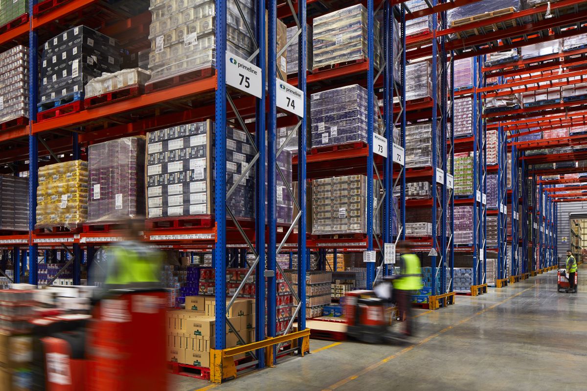 Primeline Group warehouse aisles stacked with FMCG pallets, with staff moving stock on pallet trucks